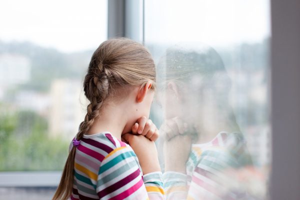 Trauriges Kind schaut aus dem Fenster des Heimes